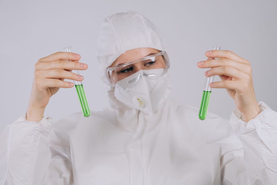 A scientist in protective gear observing green liquids in test tubes, demonstrating laboratory safety.